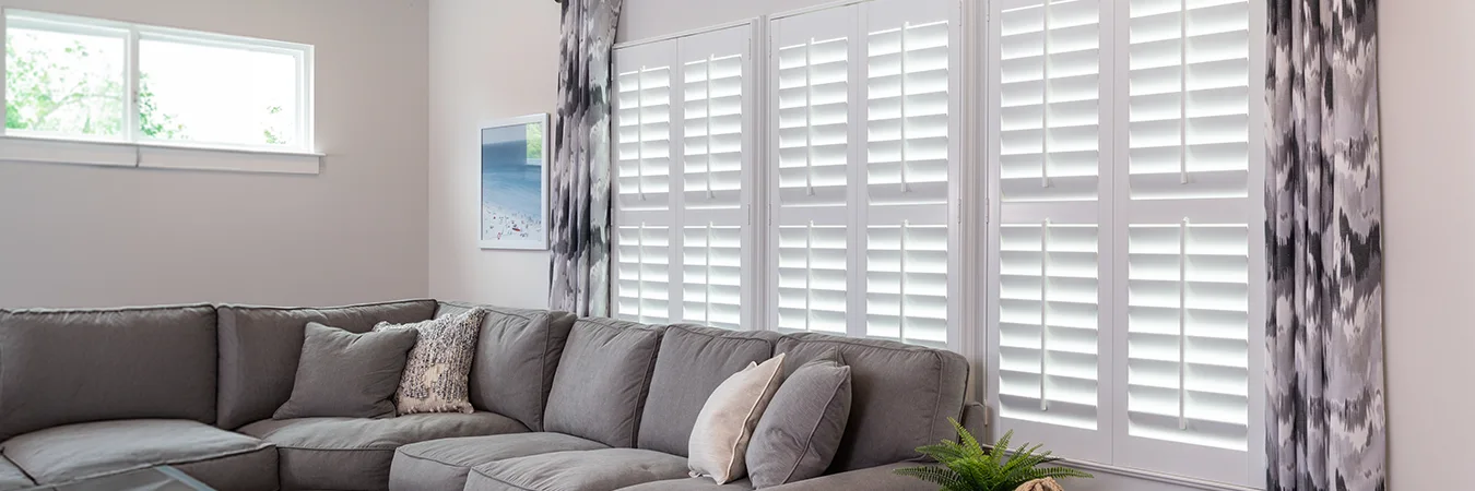 Polywood plantation shutters and patterned drapes on a large window behind a sofa