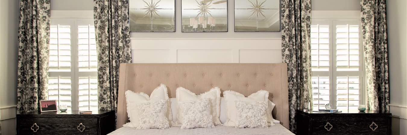 Patterned drapes framing Polywood shutters in a bedroom