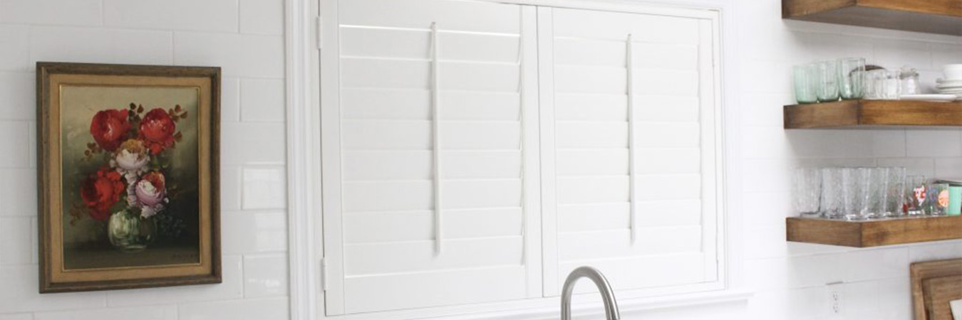 White plantation shutters with a white frame above a kitchen sink.