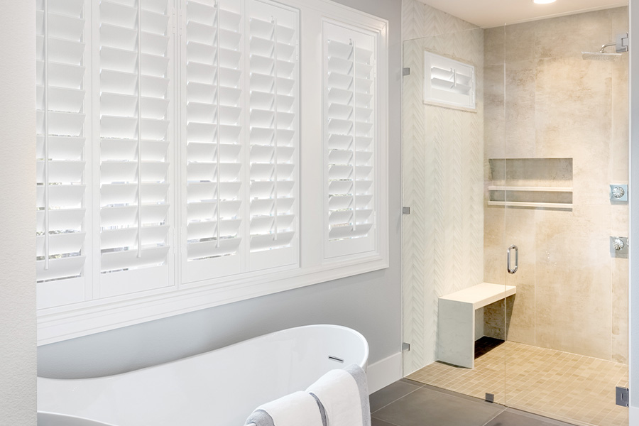 White plantation shutters with a white frame above a freestanding tub.