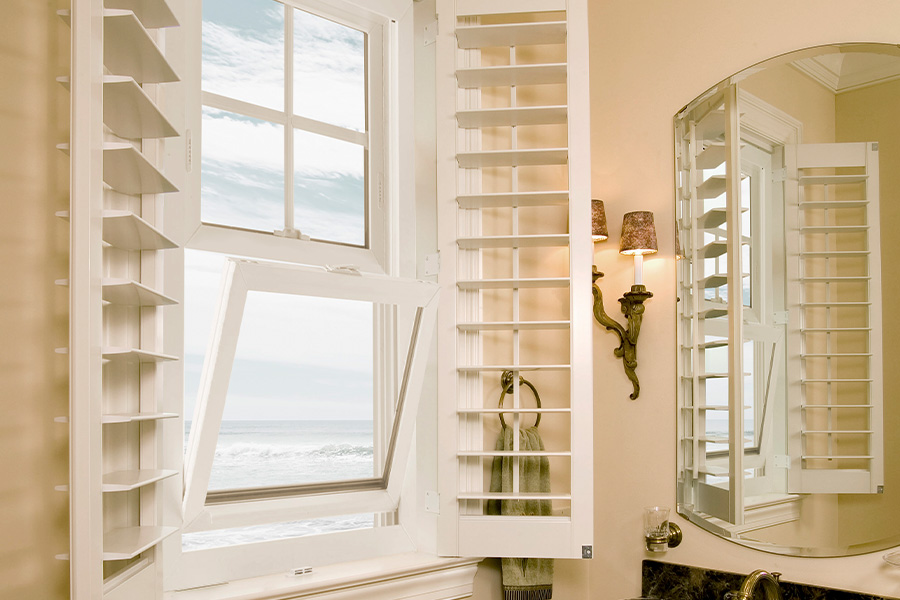 Opened shutters in a bathroom with a coastal beach scene.