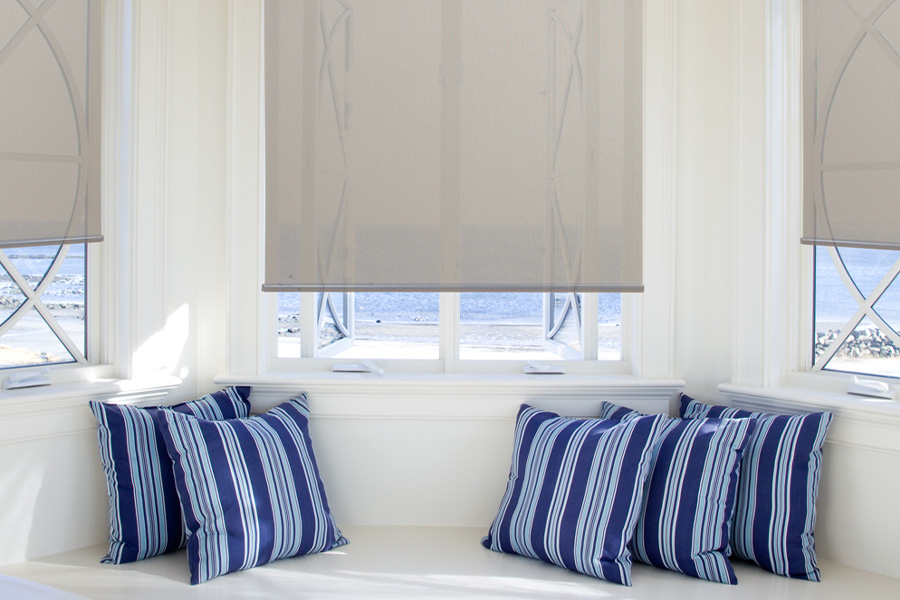Gray roller shades at a bayside window with a beach view.