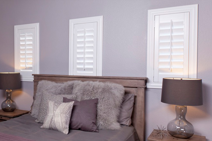White Studio shutters above a bed inside a bedroom.