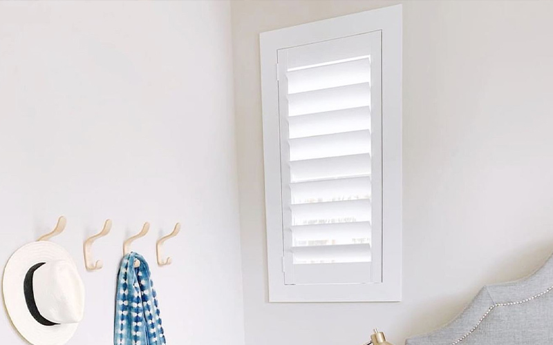 White polywood shutters by a bed.