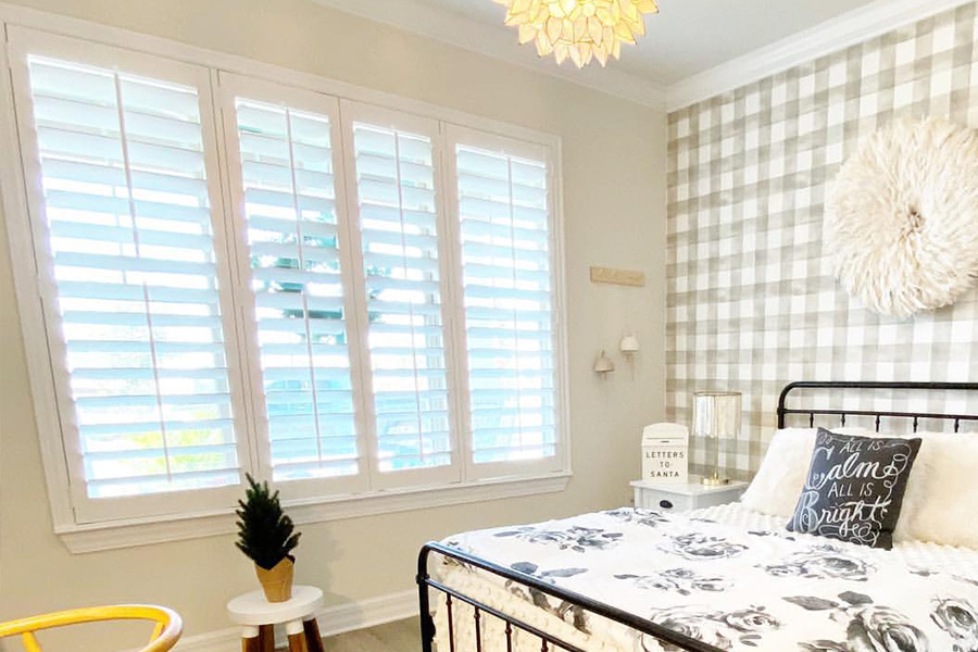White Polywood shutters on a mid-size window next to a large black and white bed.