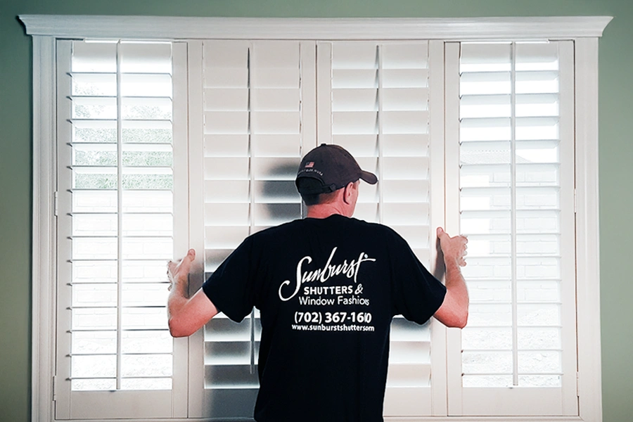 A Sunburst Shutters employee installing Polywood shutters on a window 