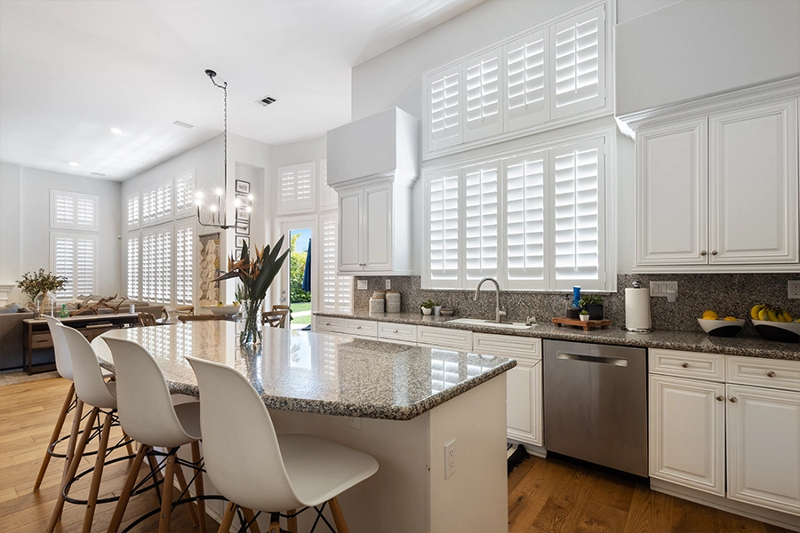 Regardless of what you call them, plantation shutters add appeal and superior light control to any room. White plantation shutters filtering light into a kitchen