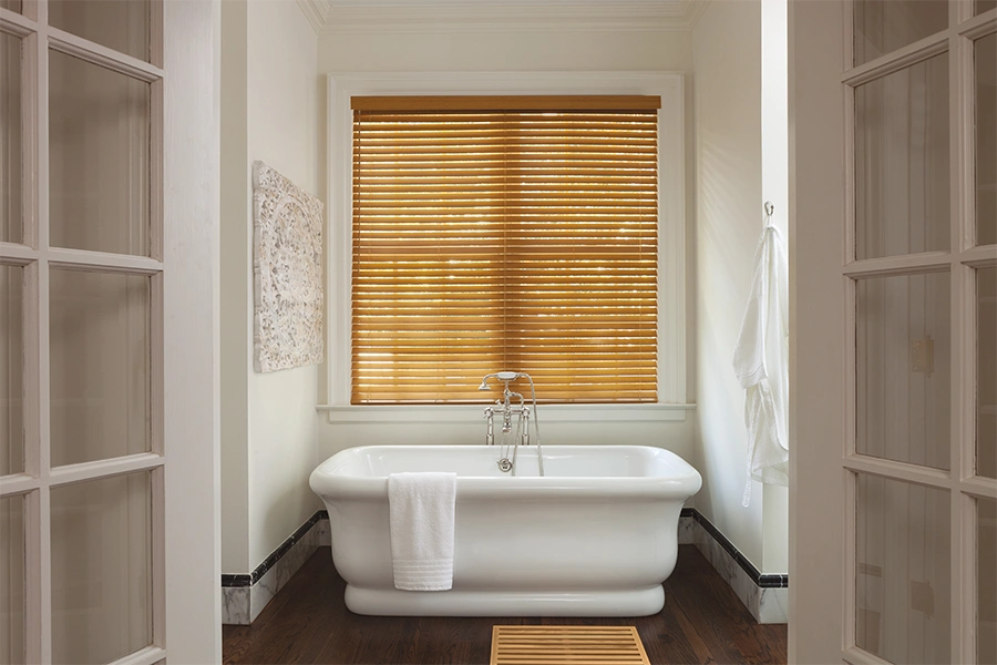 Stylish and functional, these golden oak colored window blinds work nicely in this bathroom. Golden oak colored window blinds behind a bathtub