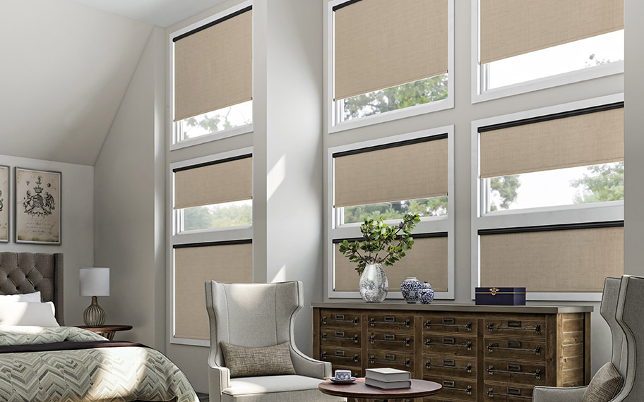 Beige motorized roller shades in a large bedroom with floor-to-ceiling windows.