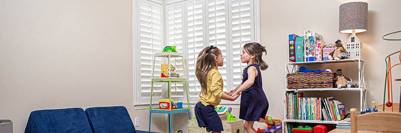 Kids playing in a large playroom with white polywood shutters in the corner.