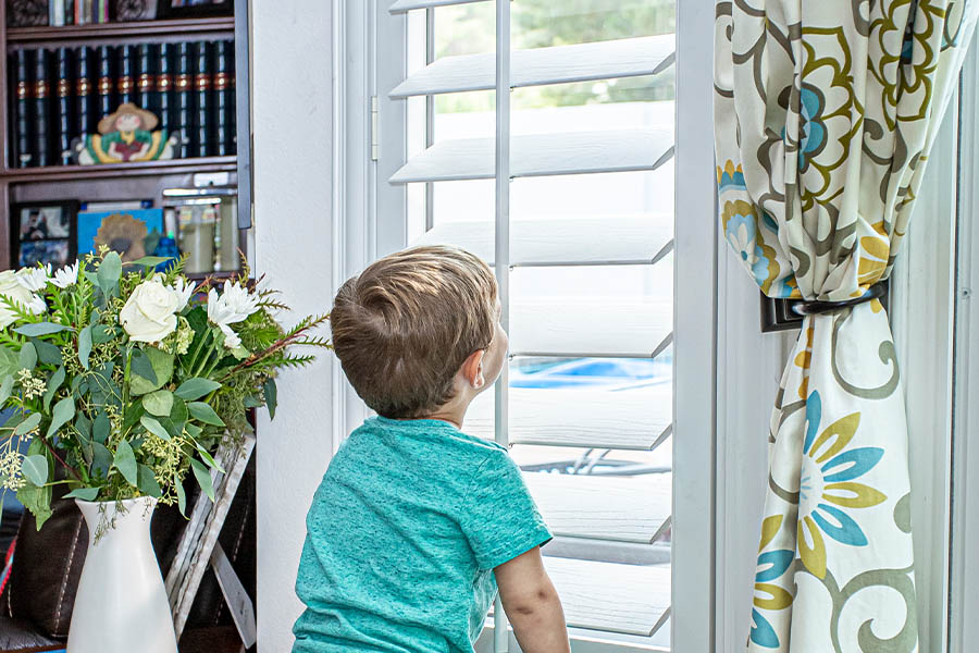 A little boy peeking through opened louver shutters.