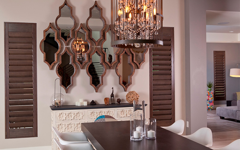 Premium wood Ovation shutters give a pop of color and texture to your Spanish-style home. Dark brown ovation shutters in a beige and brown dining room.