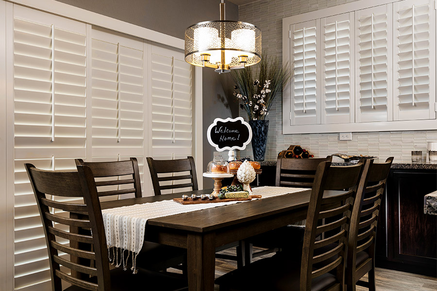 White Polywood shutters on a sliding patio door in a dining room with dark wood furniture.