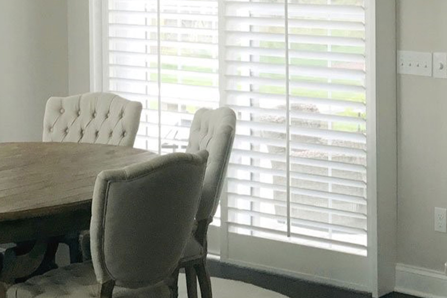 White Polywood shutters on a sliding glass door in a white dining room.