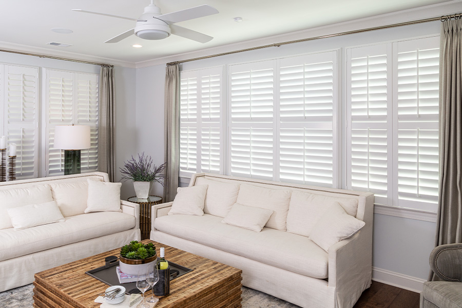 White Polywood shutters above two couches in a living room.