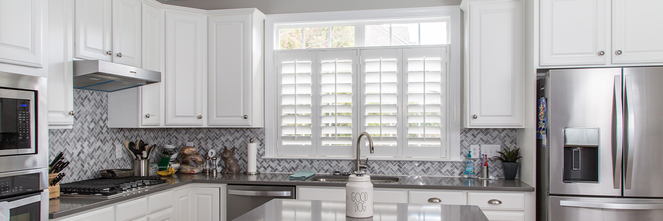 White and sleek kitchen with opened louver shutters over a kitchen sink.