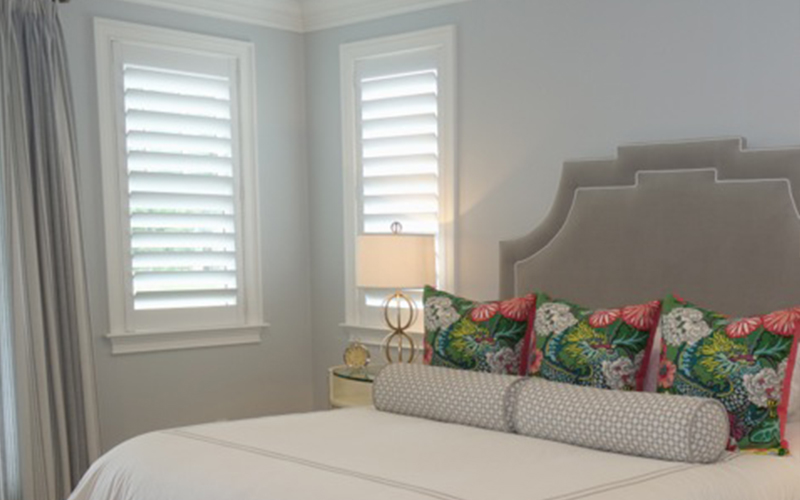 Colorful bedroom with white polywood shutters next to the bed.