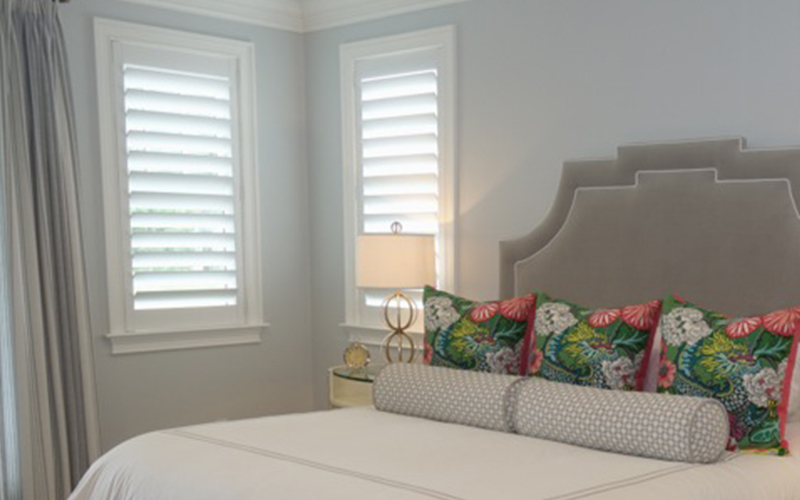 White Polywood shutters look timeless with all kinds of decor. Colorful bedroom with white polywood shutters next to the bed.