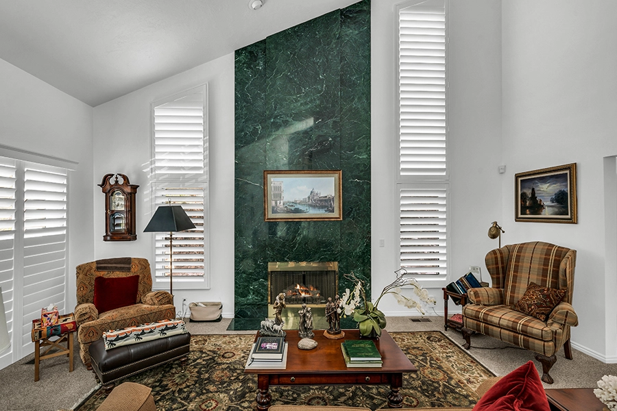 Rake window shutters framing a green, marble fireplace and mismatched chairs