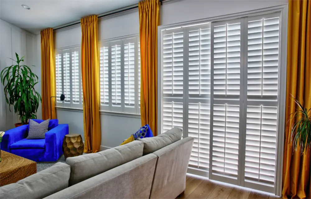 Polywood shutters are the most energy-efficient window treatments on the market and might get you a tax credit too! White polywood shutters accentuated by gold curtains in a white living room