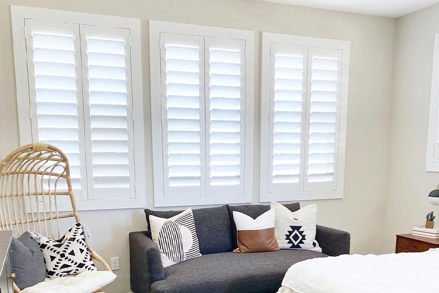 White Polywood shutters on a bedroom window over sofa and chair