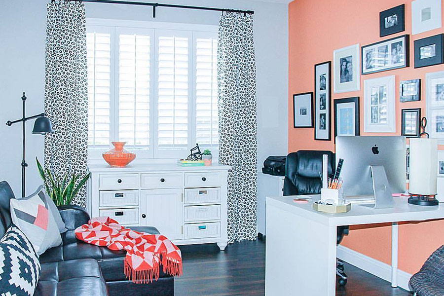 A home office with a pink accent room and white Polywood shutters on the window
