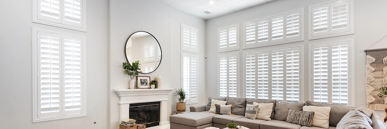 Polywood shutters on tall windows in a white living room