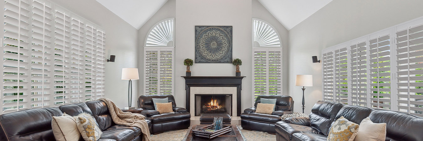 large living room with leather couches, plantation shutters, and a lit fireplace.