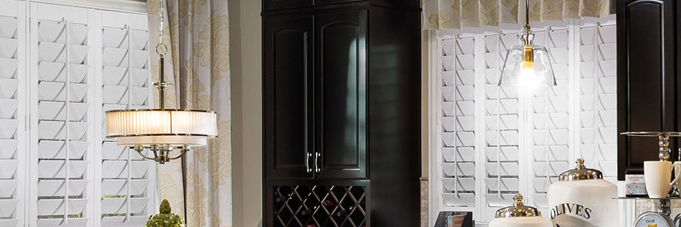 Beige valance curtain above white polywood shutters in a kitchen.