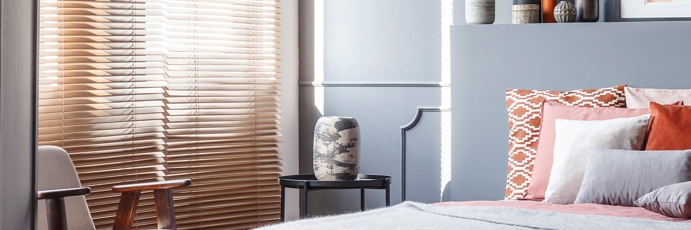 Lightly stained wood blinds in a large bedroom with gray decor.