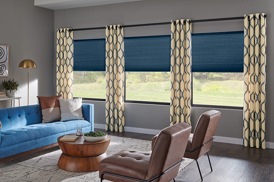 Your drapes will never look outdated when you coordinate them with other elements in the room. Beige and blue patterned drapes with blue shades on living room windows