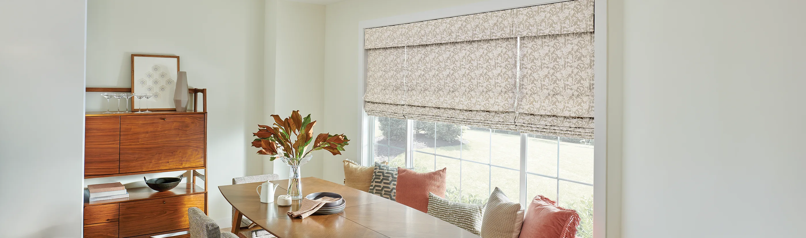 patterned biege roman shades in one large window of a dining room area
