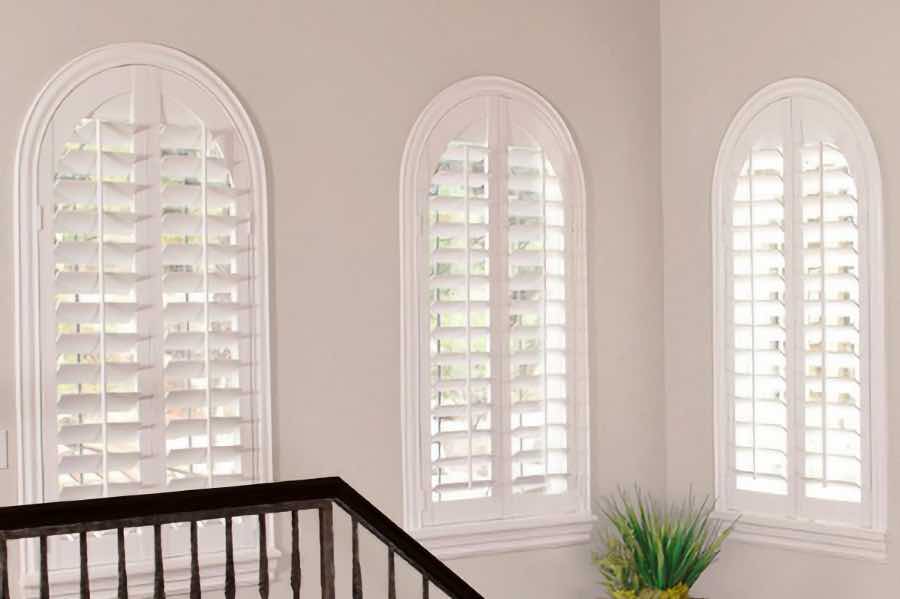 Specialty-shaped windows. High or tall windows. Not a problem. Let the experts at Sunburst measure and install your window treatments. White plantation shutters on arched windows in a stairwell