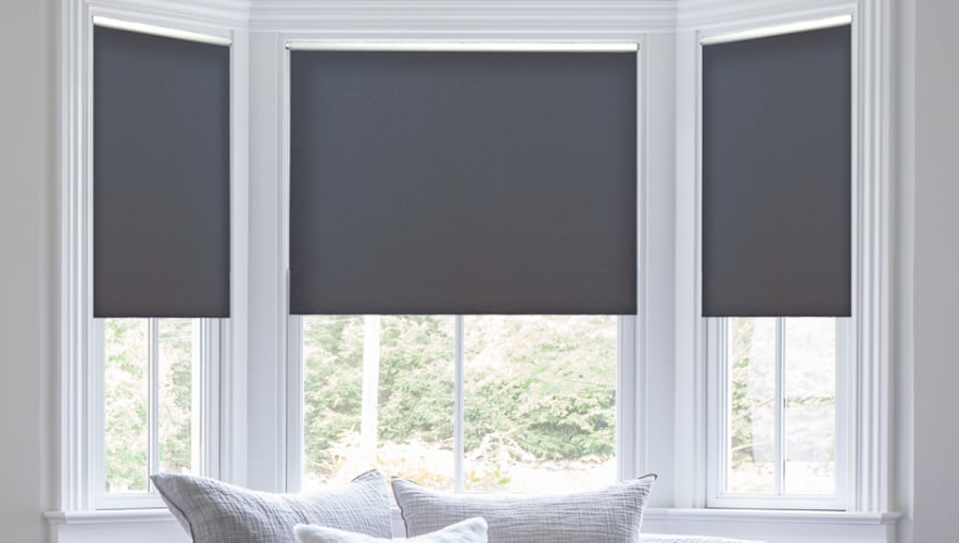 Colored roller shades are a fantastic option if you want to add a hint of color to a dull room. Dark roller shades over a window.