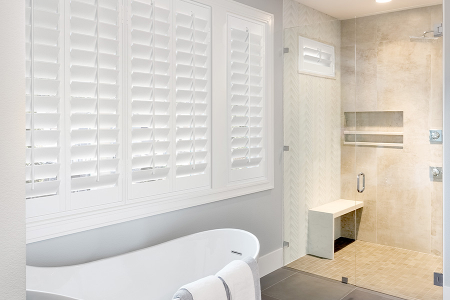 Interior shutter frames around your windows keep out cold drafts and ensure total privacy. White plantation shutters with a white frame above a freestanding tub.
