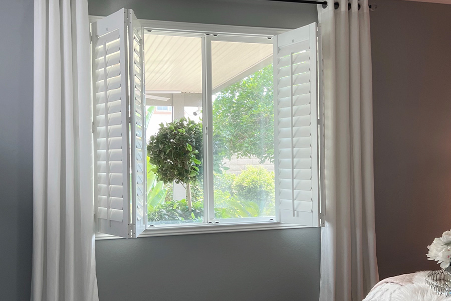 Choose between outside or inside mount frames for your plantation shutters. Folded and opened white Plantation shutters within a bedroom window.