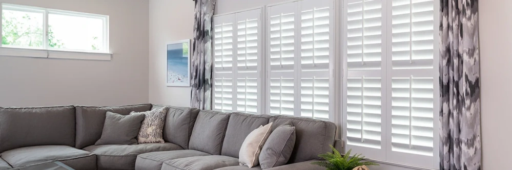 Polywood plantation shutters and patterned drapes on a large window behind a sofa