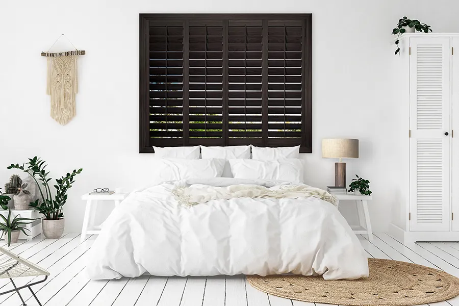 Dark wood shutters on a window above a bed with white bedding