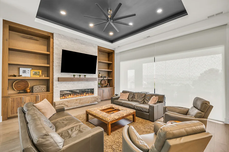 Have sun glare? Block the sun with motorized shades without missing a moment of your favorite show. Large white shades covering a wall of windows behind comfortable seating facing a big screen TV.