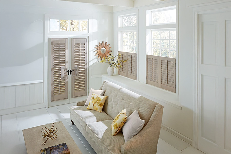 Install interior shutters on French doors for the ultimate in appeal, light control, and energy efficiency. Beige shutters on French doors and windows in a bright living space