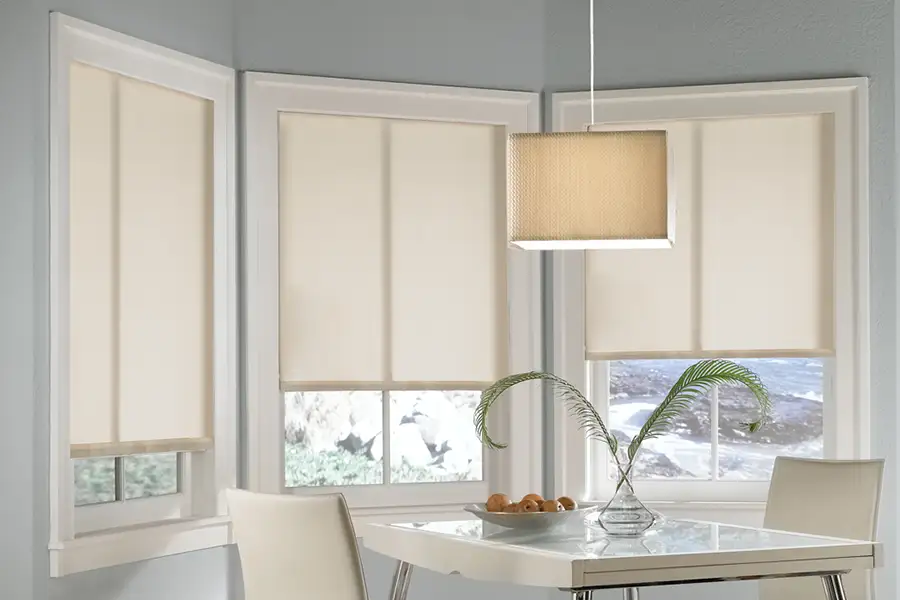 Beige roller shades on a bay window in a kitchen nook