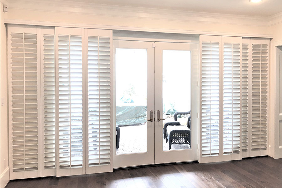 Your window treatment consultant will help you pick bypass or bi-fold shutters for your sliding door. White bypass shutters pulled to the side of a glass patio door.