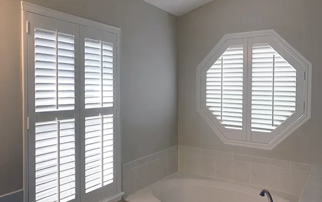 Octagon shape window with white shutters above a whirlpool tub in a bathroom