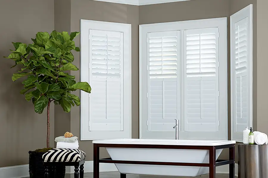 White Polywood shutters on a bay window in a brownish gray wall bathroom
