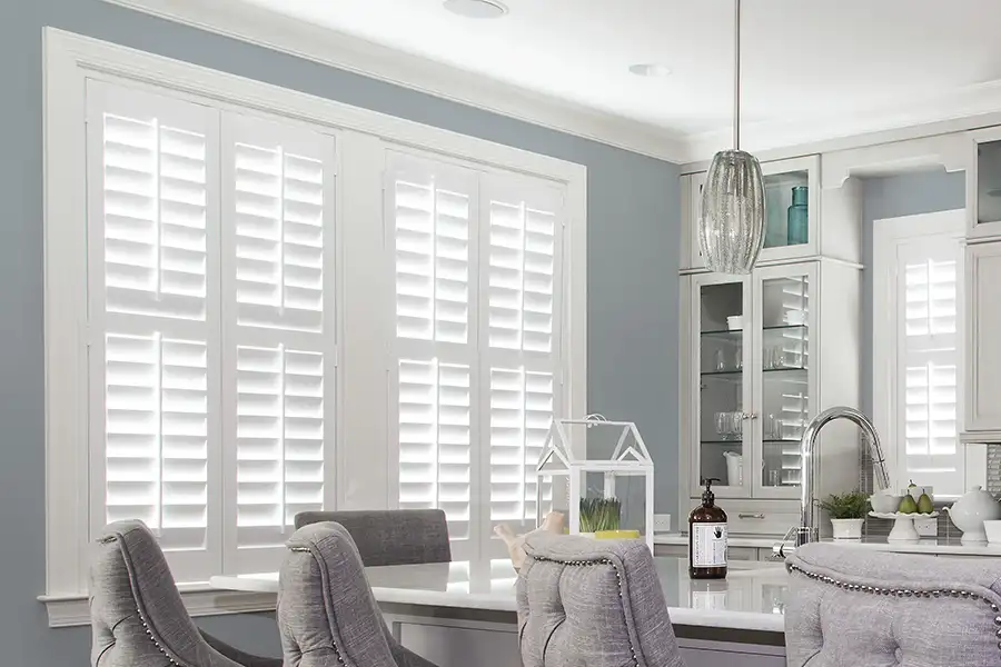 White Polywood shutters on windows in a kitchen with blue walls and white trim and cabinetry