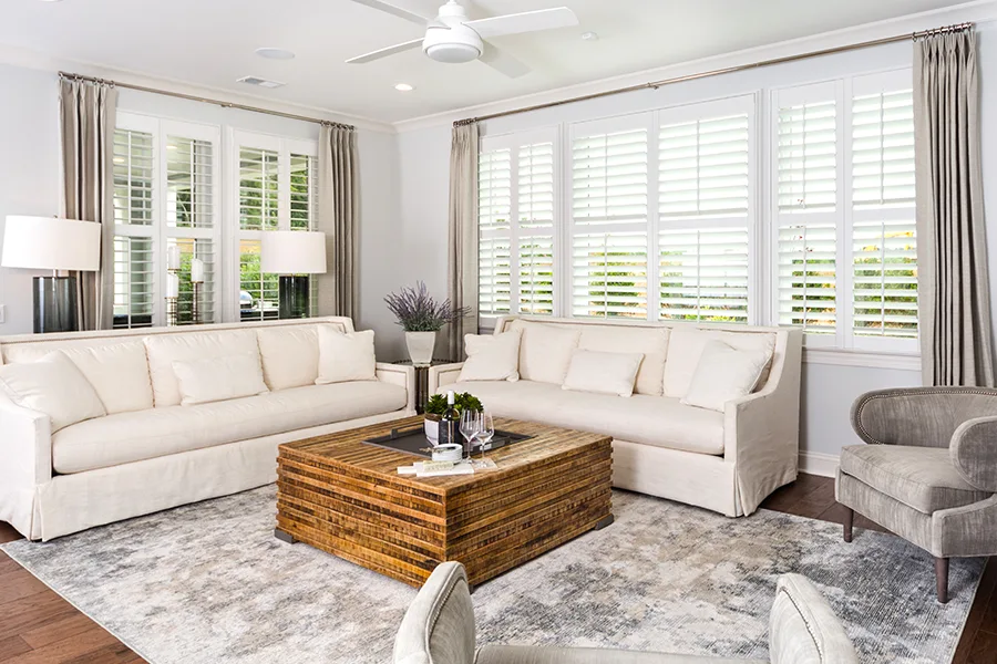 Versatile interior shutters make it easy to let in more natural light. White Polywood shutters and gray drapes on windows in a white living room