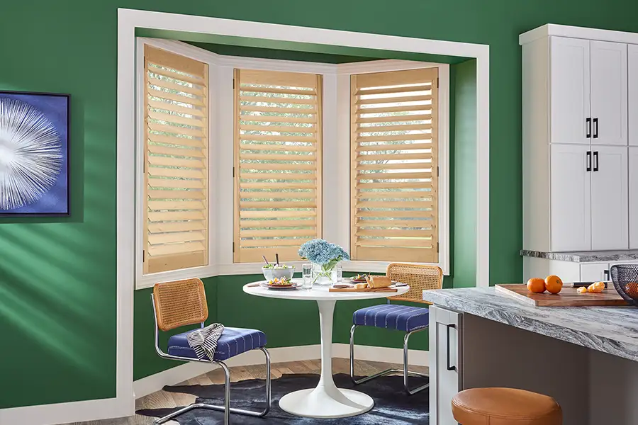 Light wood shutters within a bay window area within a breakfast nook with hunter green walls