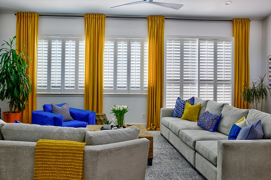 Living room with blue accent chair in front of windows and sliding glass door, covered by white plantation shutters and good drapery.